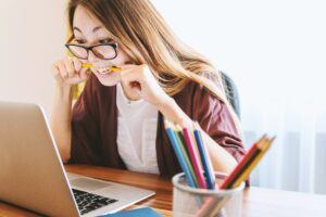 Female sitting at laptop breaking a pencil with her teeth