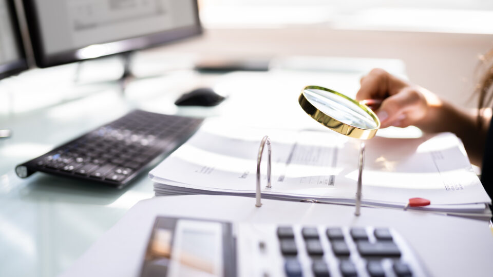 Person Examining Paper Using Magnifier Glass. Tax Fraud Investigation
